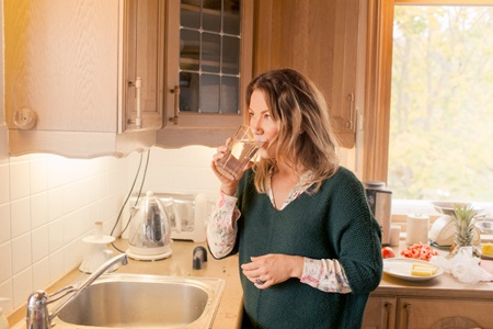 Kvinde drikker et glas vand i køkkenet, mens hun tænker over, hvordan hun er stillet ved tab af erhvervsevne.